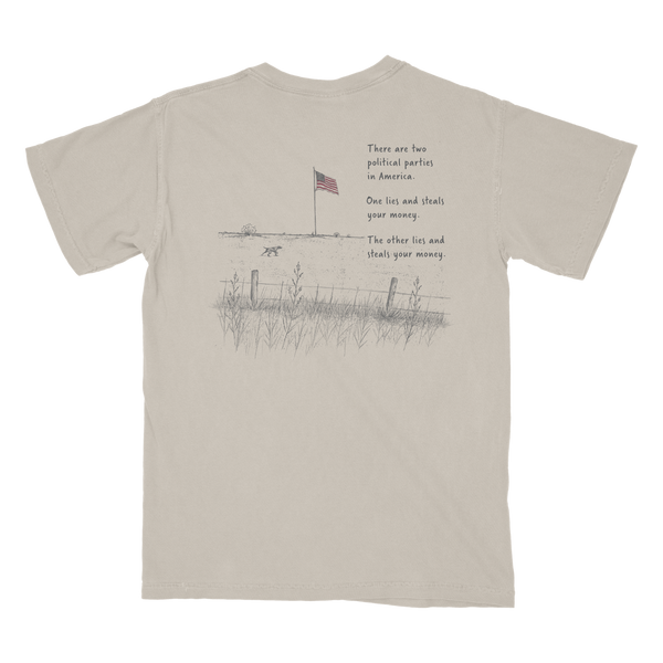 A light beige crewneck t-shirt shown from the back, featuring a black line art graphic of a rural scene with an American flag, fence, grass, and a dog, accompanied by a humorous political text print.