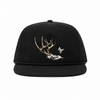 A black flat-brim snapback cap featuring a graphic of a deer skull with antlers and a small white monogram logo on the front panel, set against a plain white background.