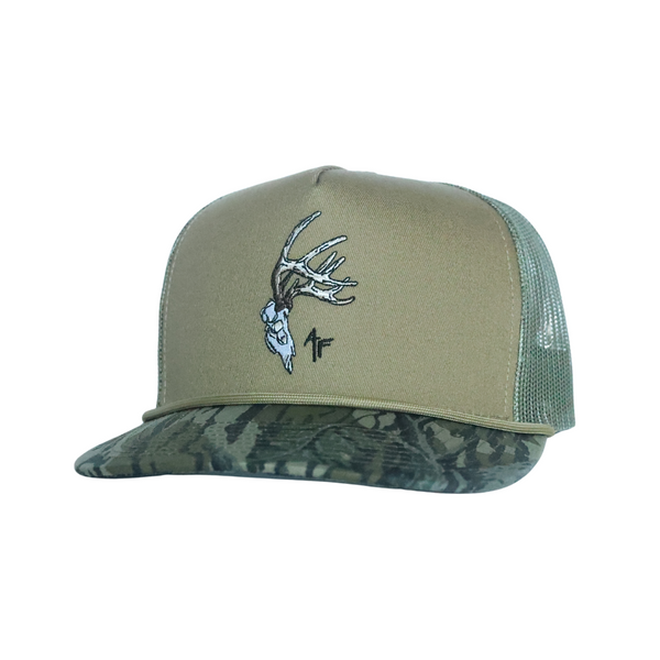 A trucker-style baseball cap with a tan front panel, green mesh back, and a camouflage patterned visor. The front panel features an embroidered deer skull with antlers and a small black 'AF logo.