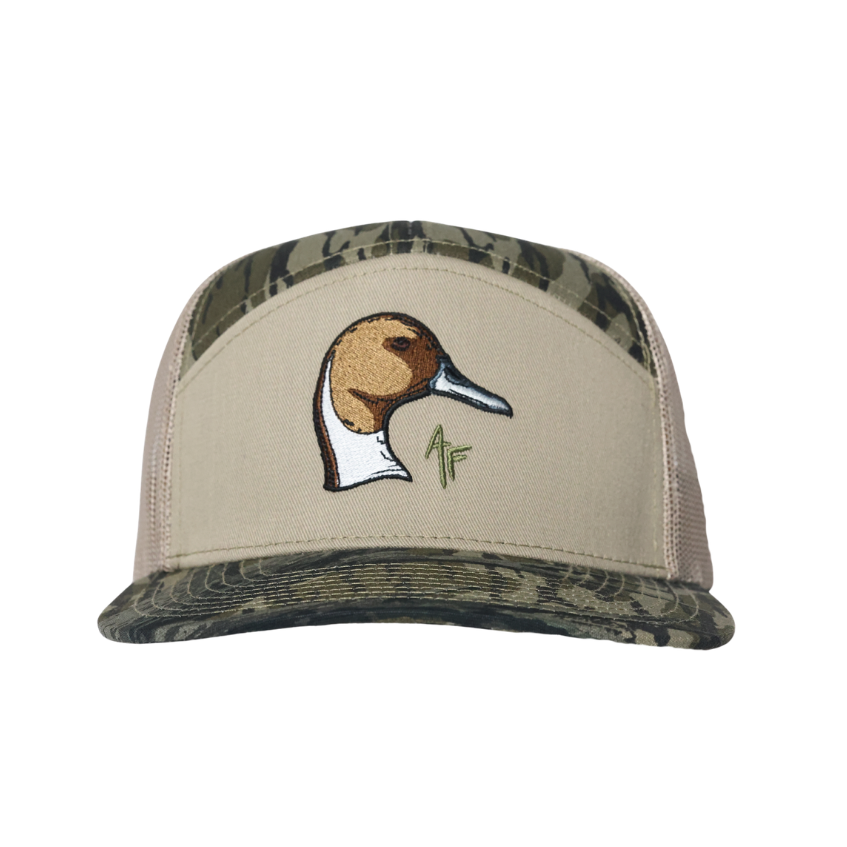 A beige trucker hat with a camouflage patterned brim and back panels, featuring an embroidered pintail duck head logo on the front.