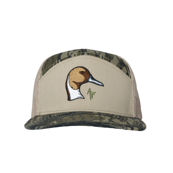 A beige trucker hat with a camouflage patterned brim and back panels, featuring an embroidered pintail duck head logo on the front.