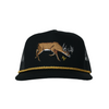 A black trucker hat with a brown embroidered deer on the front and a gold braided rope detail around the edge of the brim, shown against a plain white background.