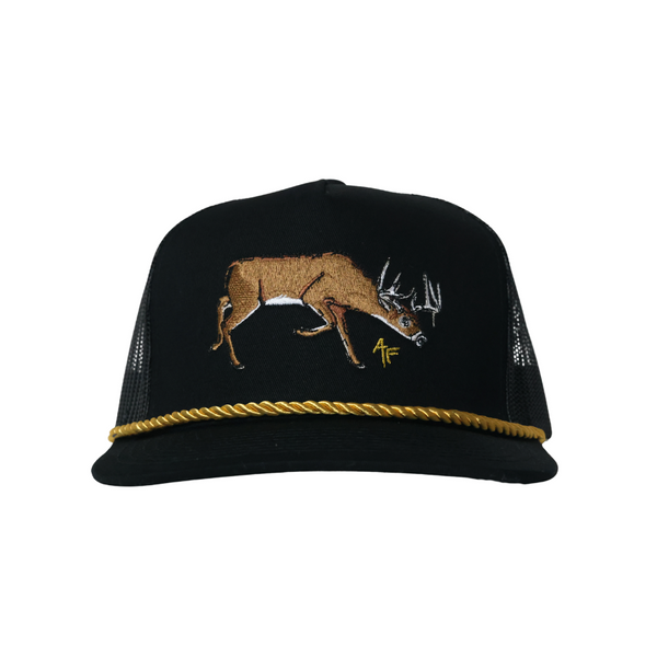 A black trucker hat with a brown embroidered deer on the front and a gold braided rope detail around the edge of the brim, shown against a plain white background.