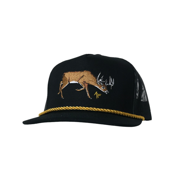 A black trucker hat with a gold braided rope detail along the brim and a brown embroidered deer on the front, shown against a plain white background.