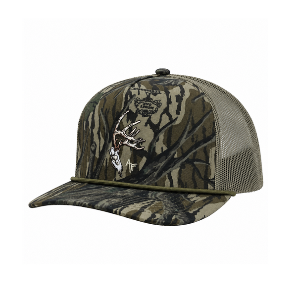 A camouflage trucker hat with a front panel featuring a realistic mossy oak tree-bark pattern, olive green mesh back, and a silver deer head logo embroidered on the front.