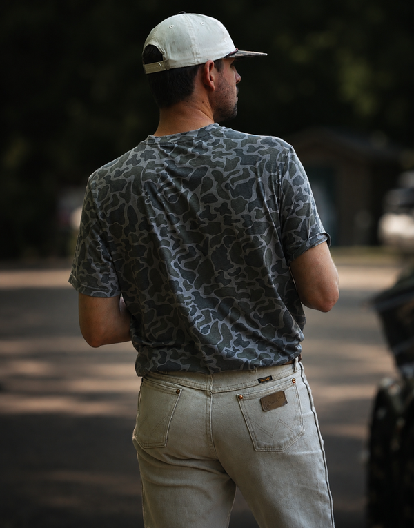 Man wearing a patterned shirt and cap, standing outdoors with a blurred background